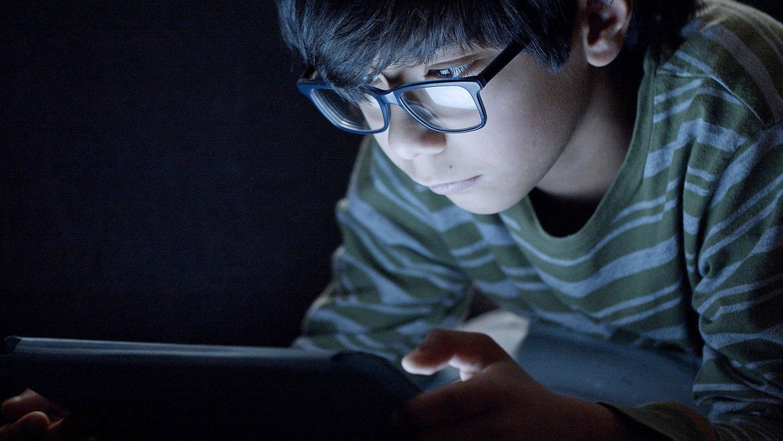 Jongen met bril kijkt naar een tablet in het donker