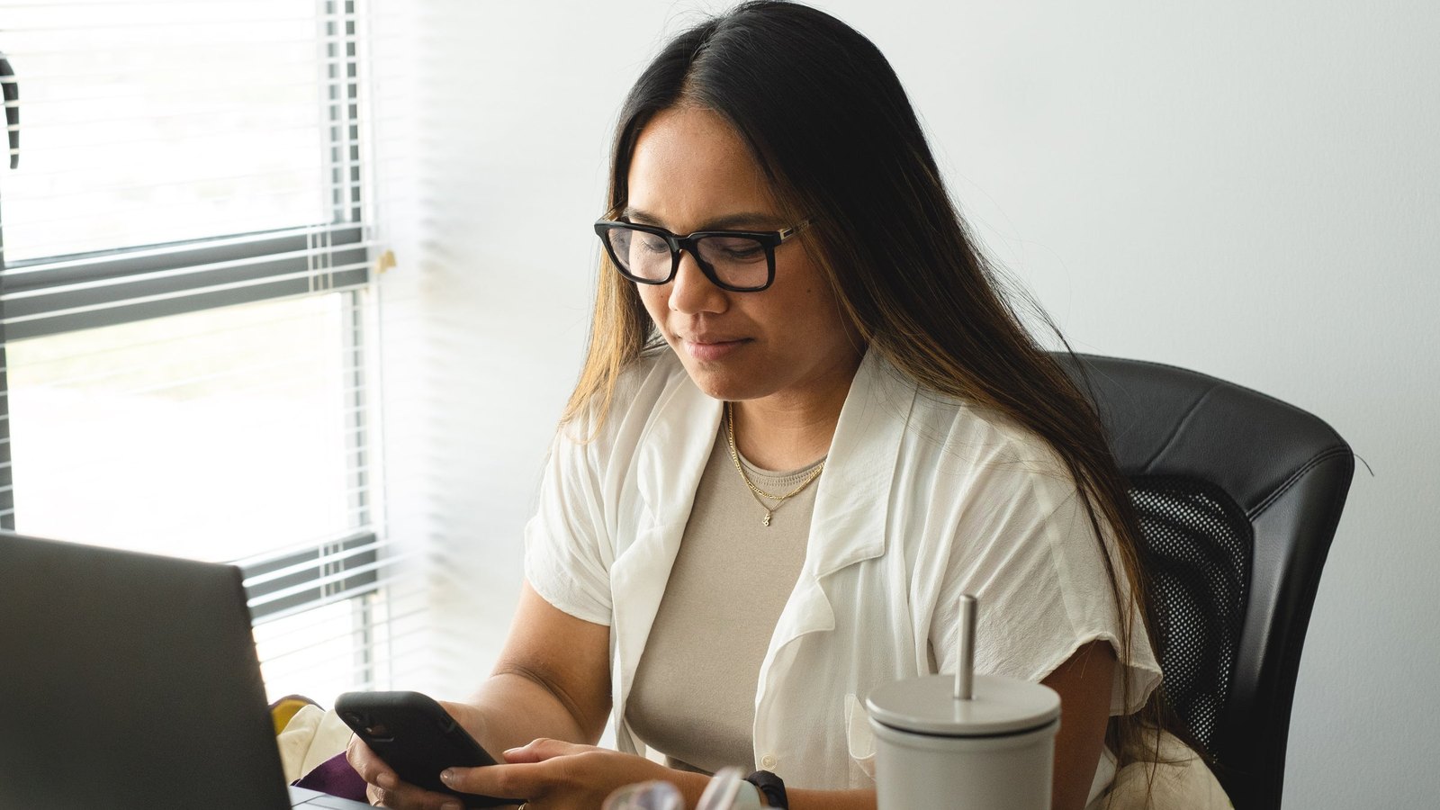 Vrouw met bril werkt achter een laptop bij het raam