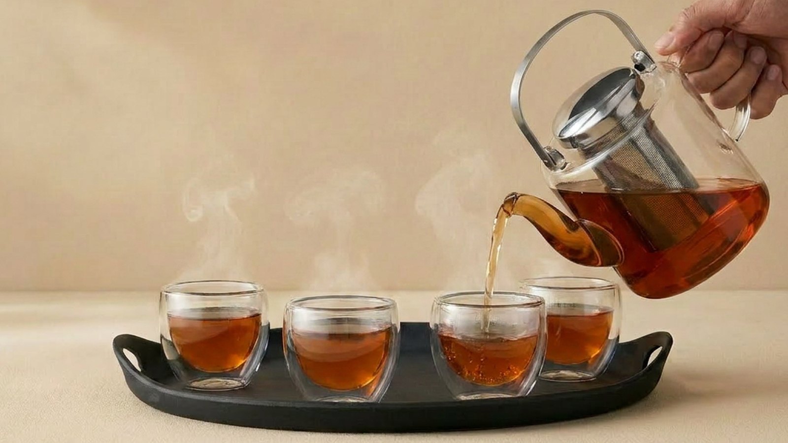 Glazen theepot met kruidenthee wordt uitgeschonken in vier glazen op een zwart dienblad