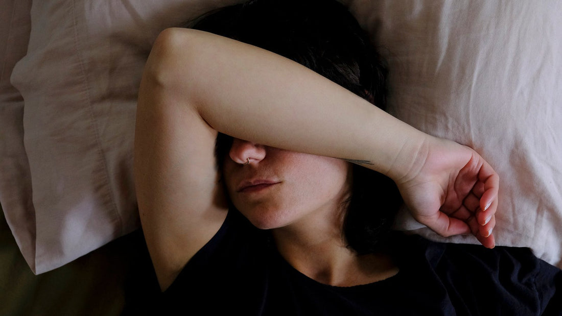 Vrouw ligt in bed met haar arm over haar ogen