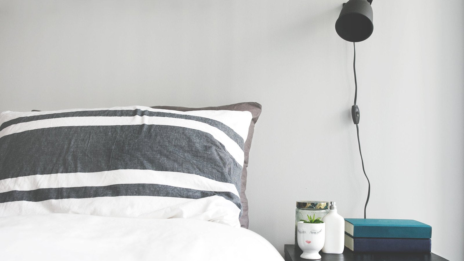 Opgemaakt bed met een nachtkastje en een klein potje