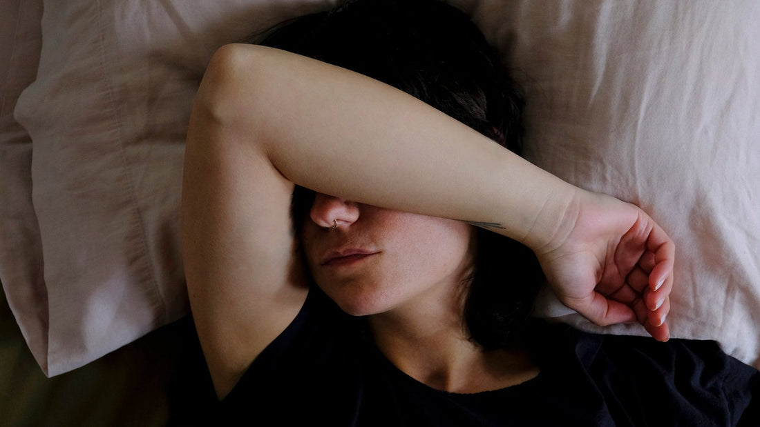Vrouw ligt in bed met haar arm over haar ogen en haar mond gesloten