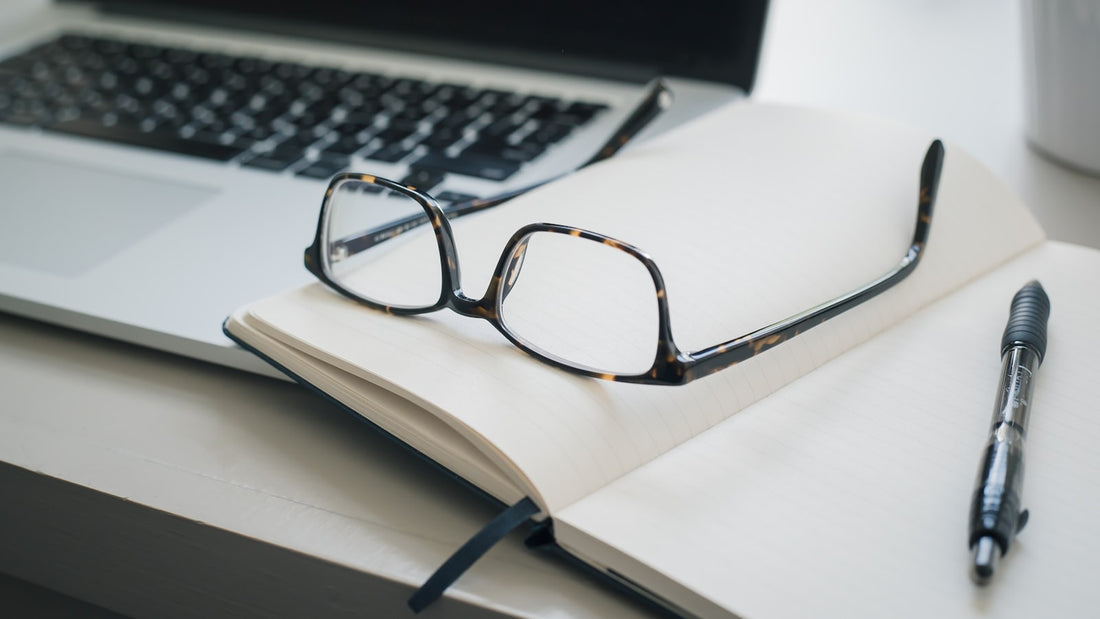 Bril op een notitieboek naast een laptop