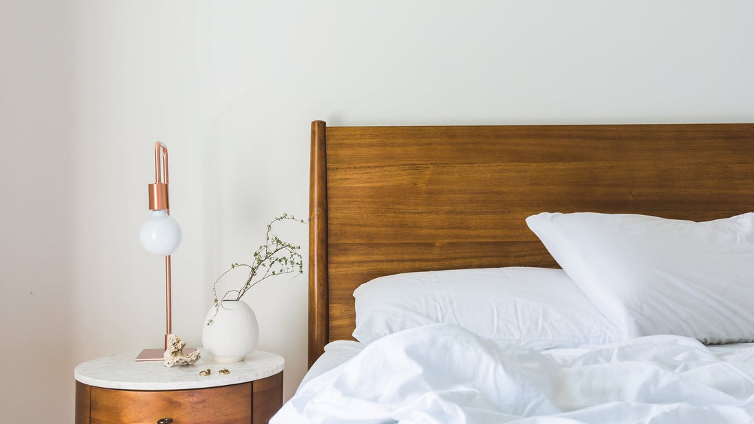 Rustige slaapkamer met een houten hoofdbord, wit beddengoed en een warme lamp