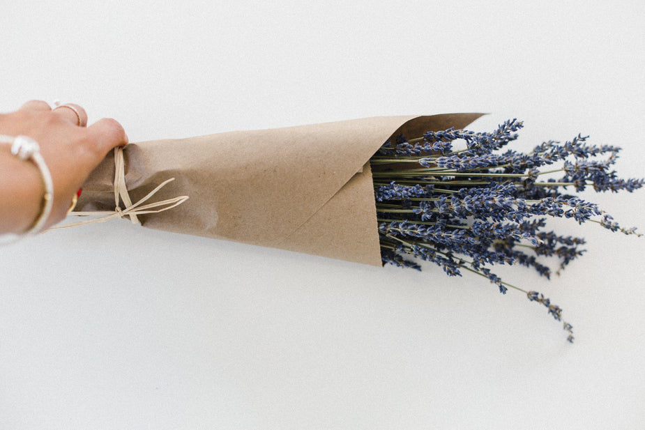 Hand houdt bosje lavendel in kraftpapier vast